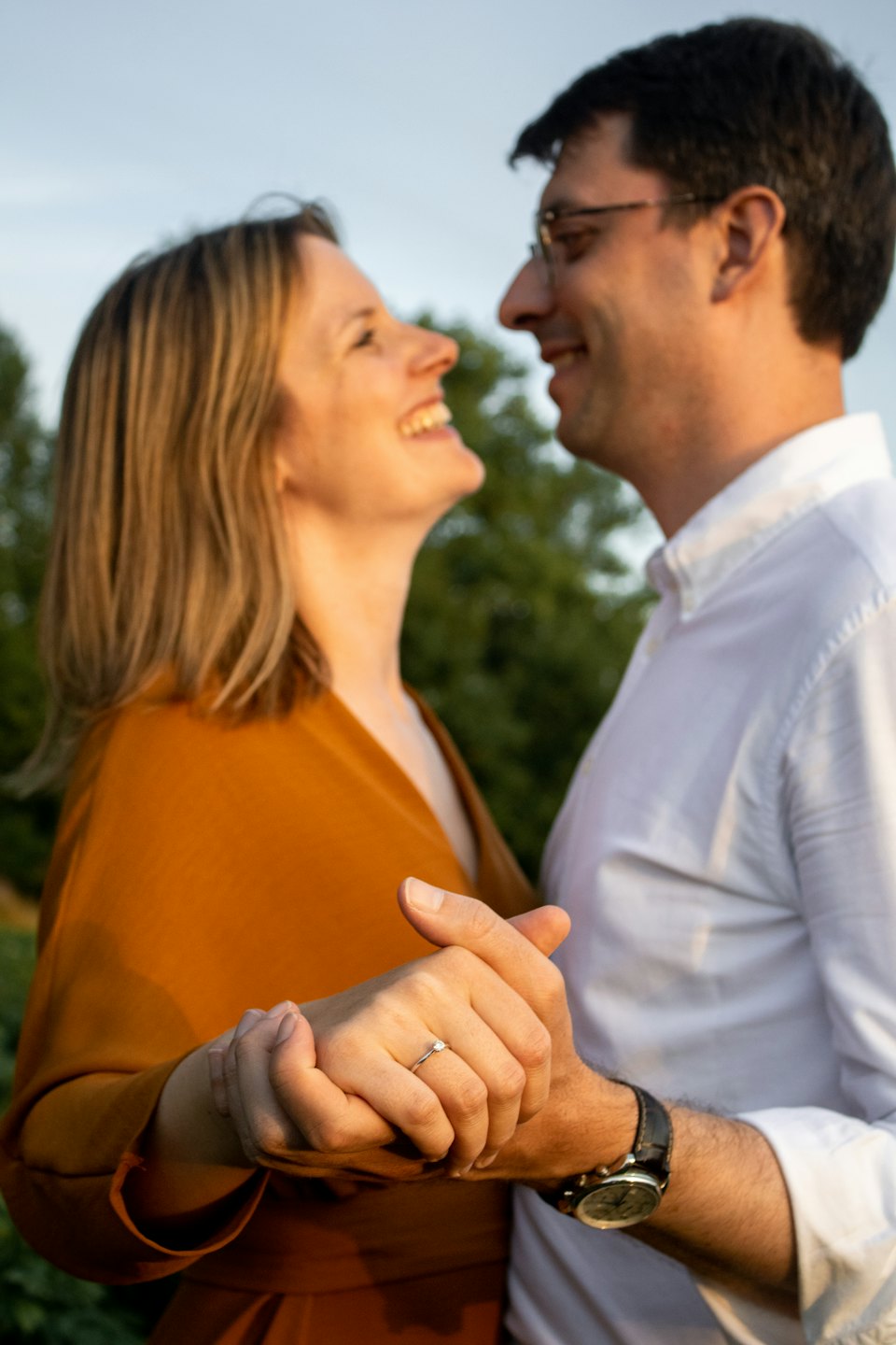 A couple holds hands and smiles at each other outdoors.