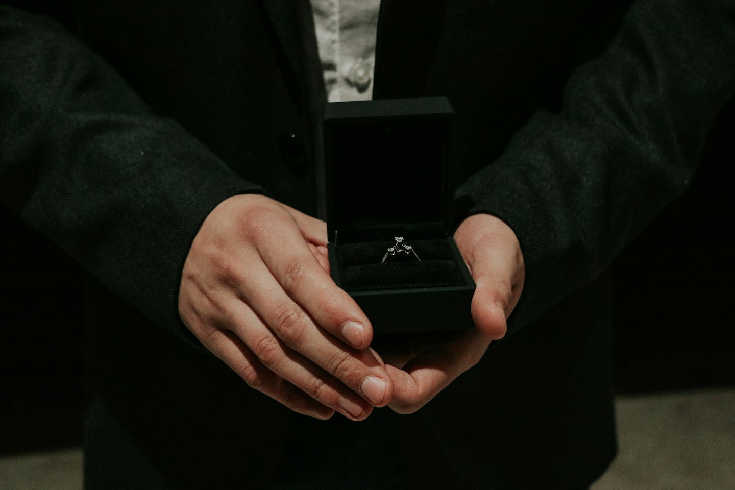 Hands in a suit jacket hold an open engagement ring box.
