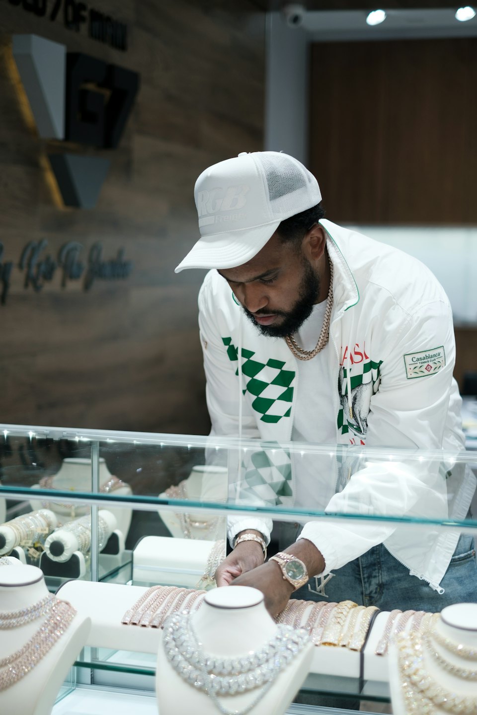 Man in white jacket inspects jewelry in a glass case.